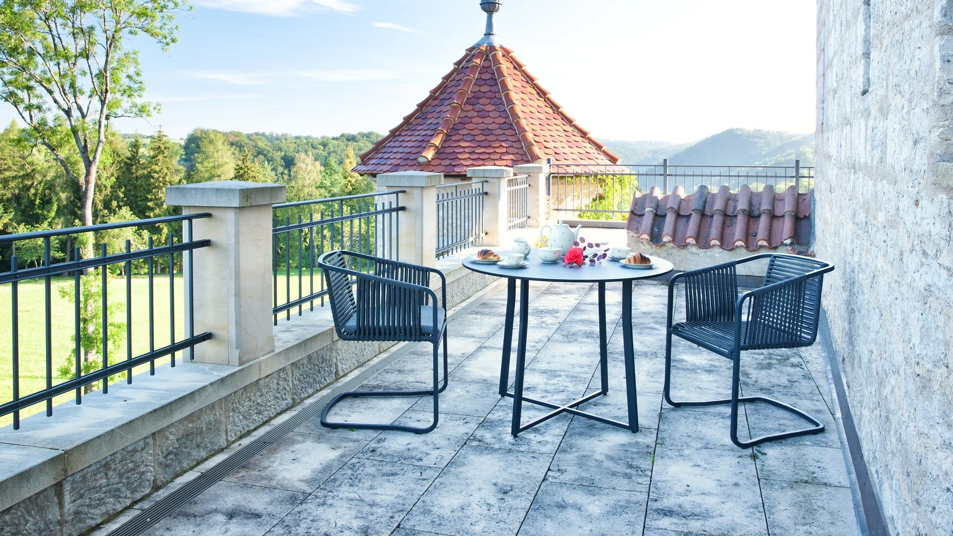Suite Bar-Set bestehend aus einem hohen Bartisch und Barstühlen auf einem Holzdeck mit Glasreling und weitem Ausblick.