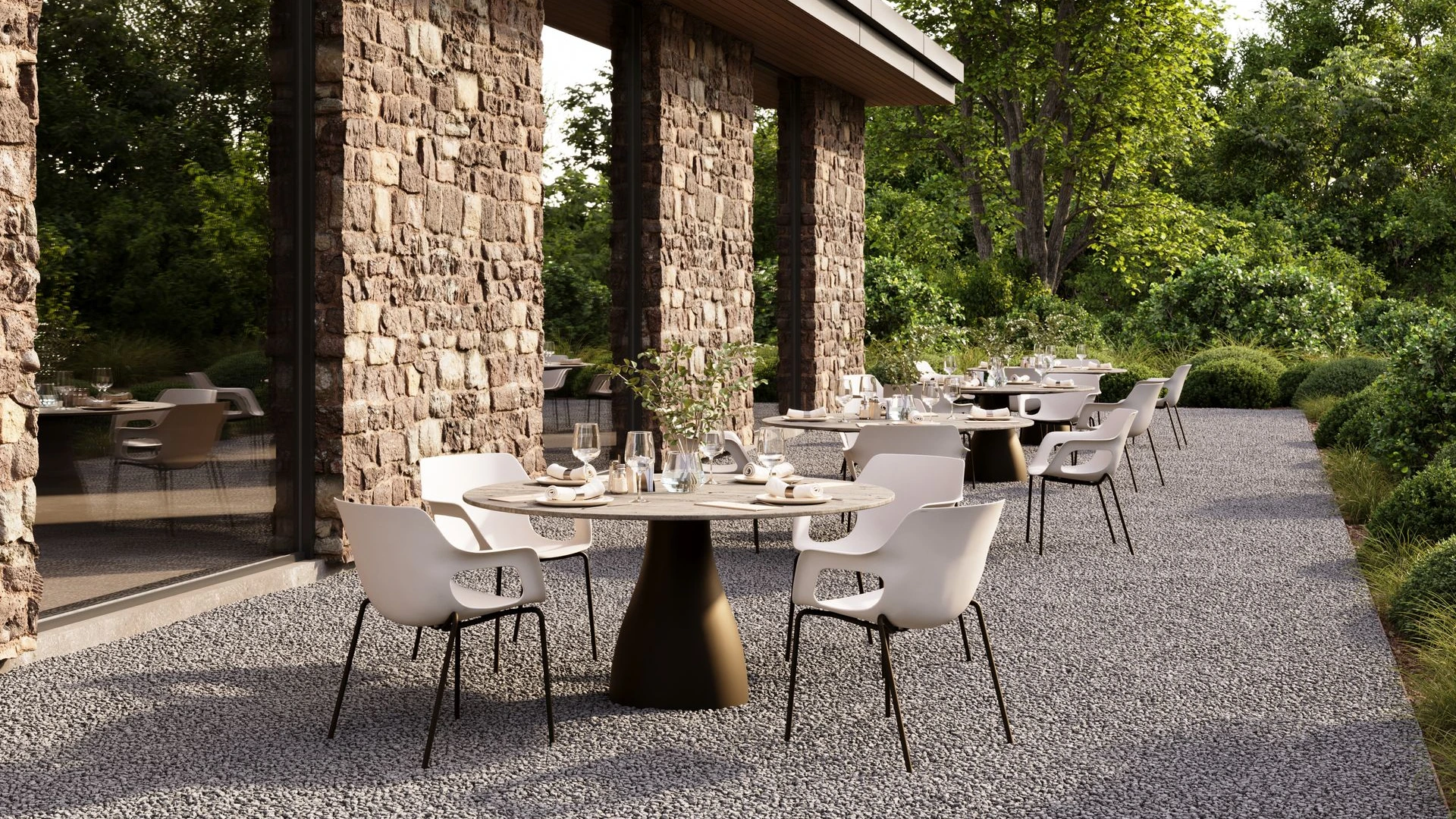 Runder Monroe Säulentisch in Dark Bronze mit FM-Ceramtop-Platte, flankiert von zwei Tempus Schalensesseln in Crema und Dark Bronze auf einer Terrasse.